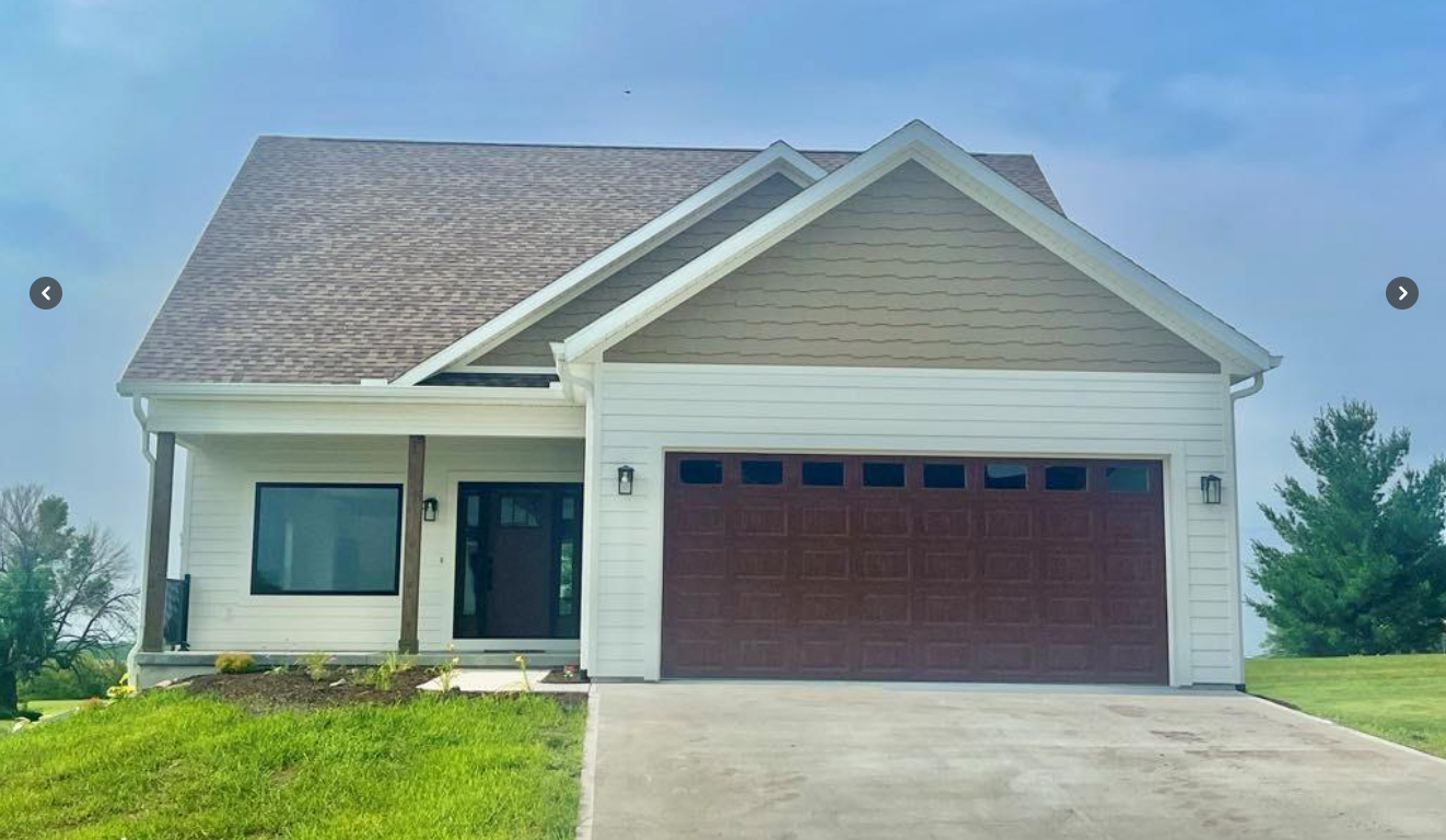 Single-story suburban house with beige siding, brown garage door, and a green lawn under a clear sky