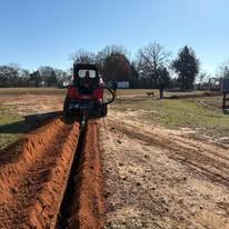A tractor is digging a trench in the dirt in a field.