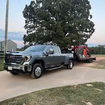 A truck is towing a tractor down a road.