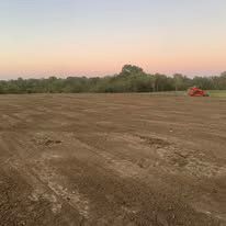 A large dirt field with a tractor in the background.