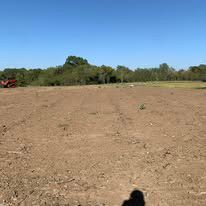 A tractor is plowing a field with trees in the background on a sunny day.