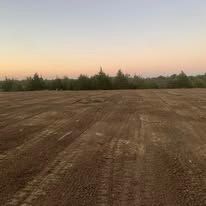A large dirt field with trees in the background at sunset.