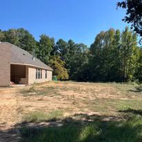 A house is sitting in the middle of a dirt field surrounded by trees.