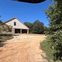 A white barn is sitting on top of a dirt road surrounded by trees.