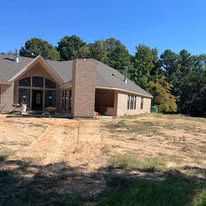 A large house is sitting on top of a dirt hill surrounded by trees.