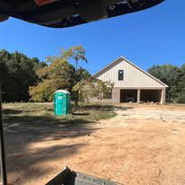 A green portable toilet is in front of a house under construction.