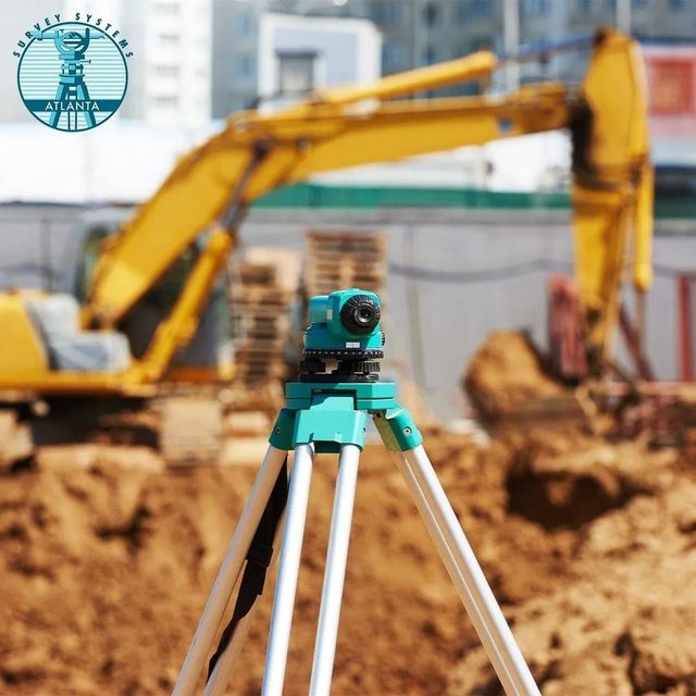 Survey level tripod on a construction site with excavator in the background.