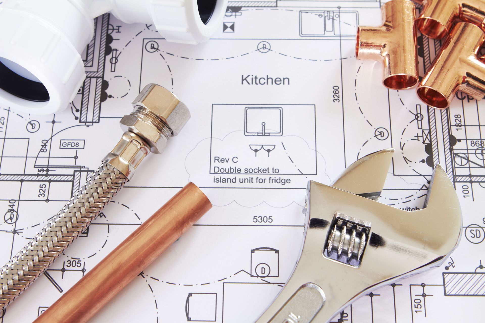 Plumbing tools and parts (wrench, flexible hose, pipes) on top of a blueprint of a kitchen.