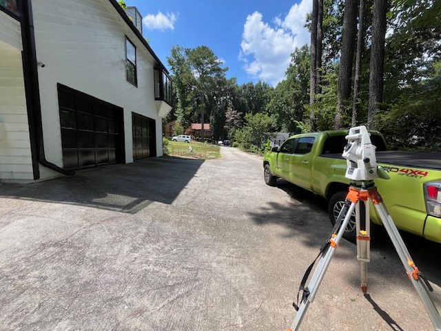 Lime green truck with surveying equipment set up on asphalt driveway near a white building and treeline.