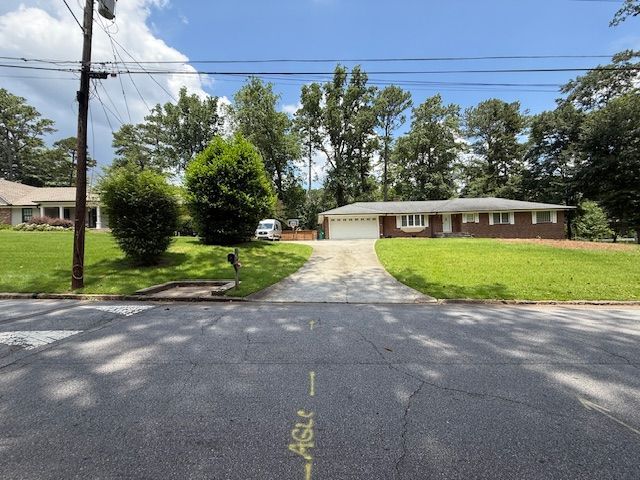 A single-story brick house with a driveway and green lawn on a sunny day.