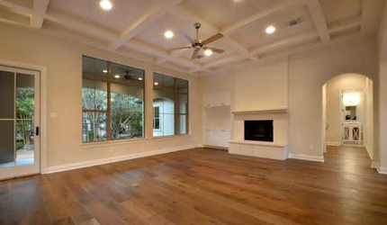An empty living room with hardwood floors , a fireplace and a ceiling fan.