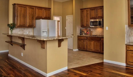 A kitchen with wooden cabinets , granite counter tops , a refrigerator and a microwave.