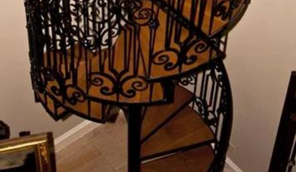 A wooden spiral staircase with a wrought iron railing in a room.