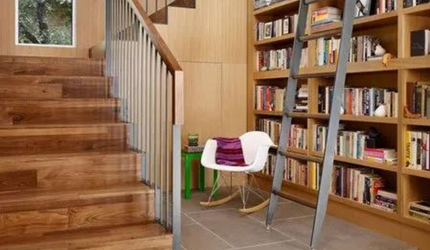 A wooden staircase leading up to a bookshelf with a ladder.