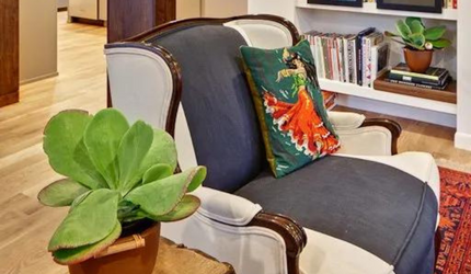 A chair with a pillow on it is in a living room next to a potted plant.