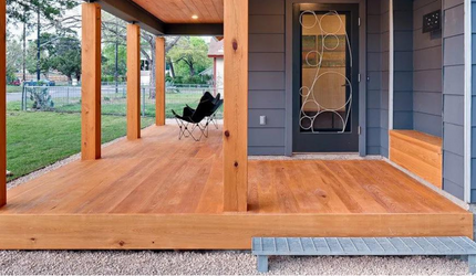 A wooden porch with a chair on it in front of a house.