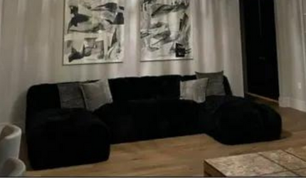 A living room with a black couch and two paintings on the wall.