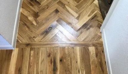 A wooden floor with a herringbone pattern in a hallway.
