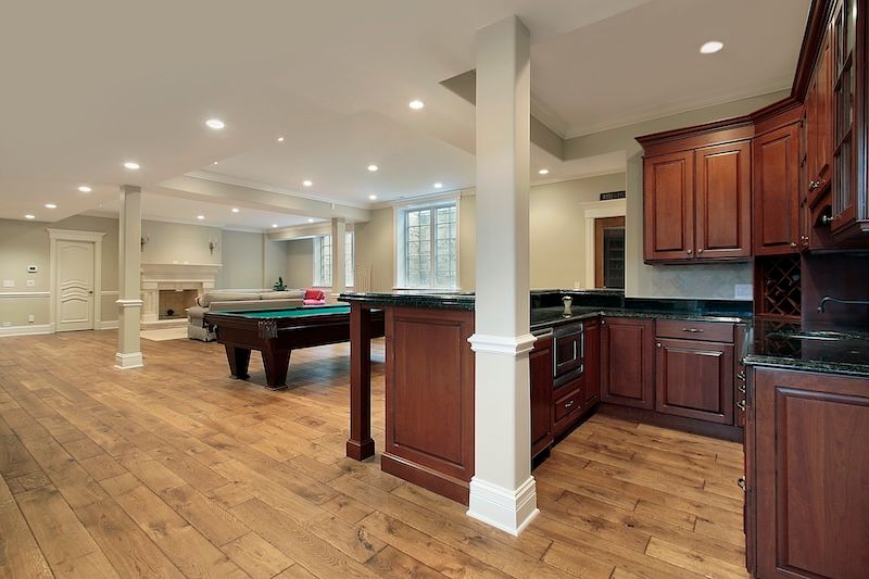 A basement with hardwood floors , a pool table , and a kitchen.