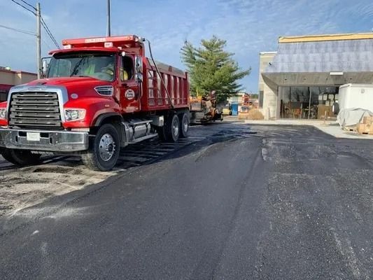 A bright red dump truck parked on a newly paved asphalt lot in front of a building under construction.