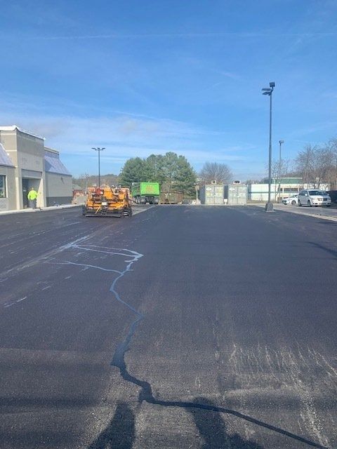 Construction equipment paving a commercial parking lot under a bright blue sky.