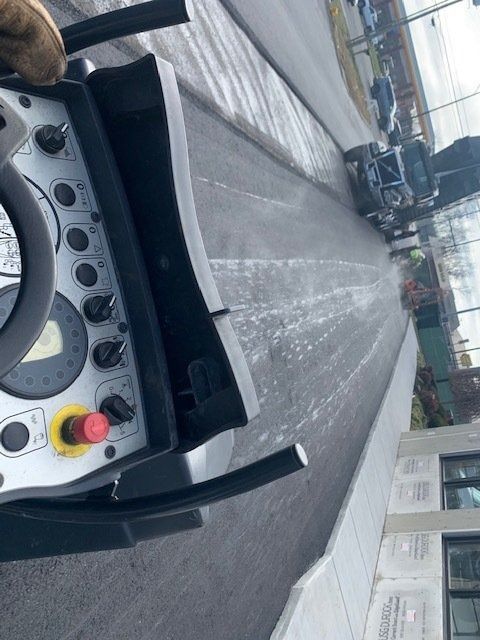 A first-person view from a paving machine operator’s station looking out at a freshly paved dark asphalt road.