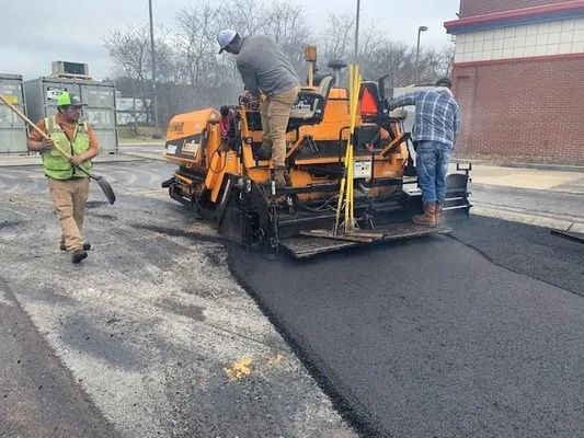A construction crew operates an asphalt paving machine on a road surface.