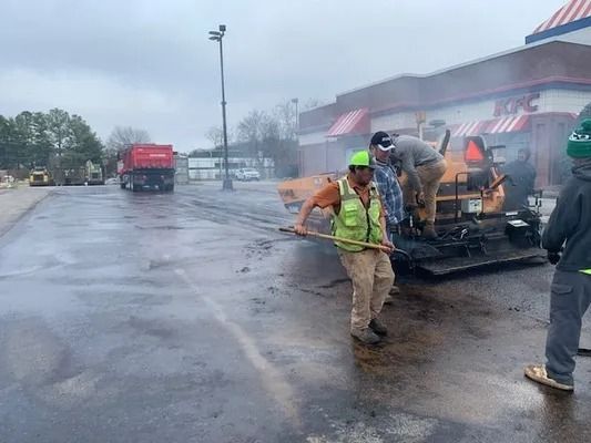 Construction workers operate a paving machine to resurface a parking lot in front of a KFC restaurant.