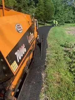 An orange LeeBoy 7000C asphalt paver laying down a new path outdoors with workers standing in the distance.