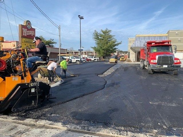 Construction workers using a yellow asphalt paving machine to resurface a parking lot next to a Wendy’s restaurant.