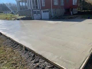 Freshly poured concrete driveway in front of a red house with a wooden frame along the edge.
