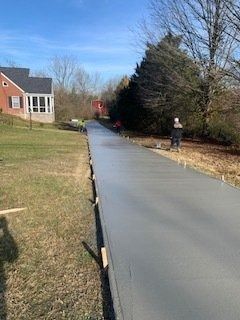 Workers finishing a freshly poured concrete driveway leading toward a house on a sunny day.