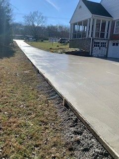 A newly poured concrete driveway extends alongside a grassy yard toward a house with a screened porch.