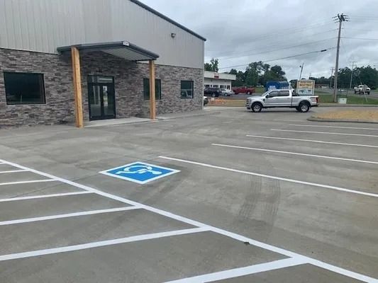 A building exterior with a paved parking lot featuring a blue and white accessible parking symbol and striped safety zones.