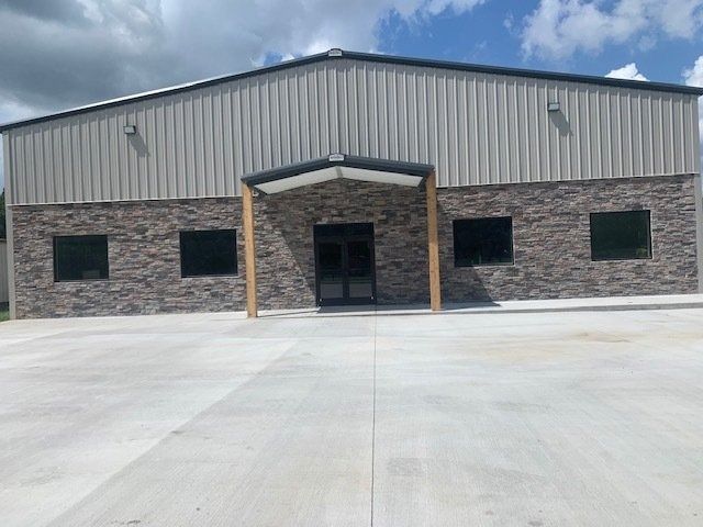 A commercial building with a beige metal upper half and a stone veneer lower half, featuring a centered glass entrance.