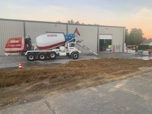 An SRM concrete mixer truck parked in front of a warehouse building, with a patriotic flag design on its drum.