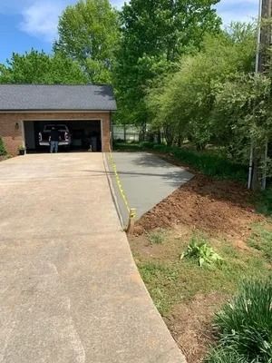 A freshly poured concrete driveway extension next to an existing driveway and a garage with an open door.