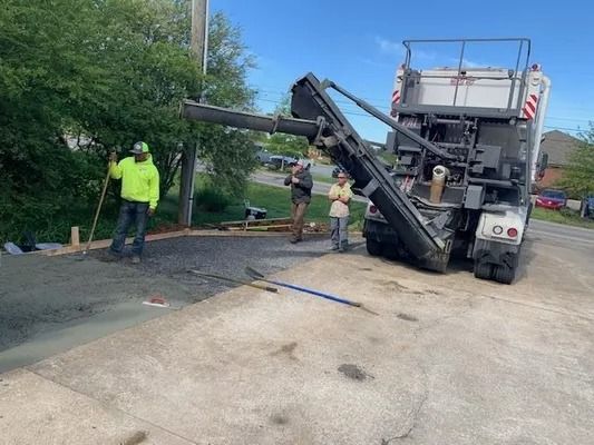 Three workers pour concrete from a truck mixer onto a residential driveway construction site on a sunny day.
