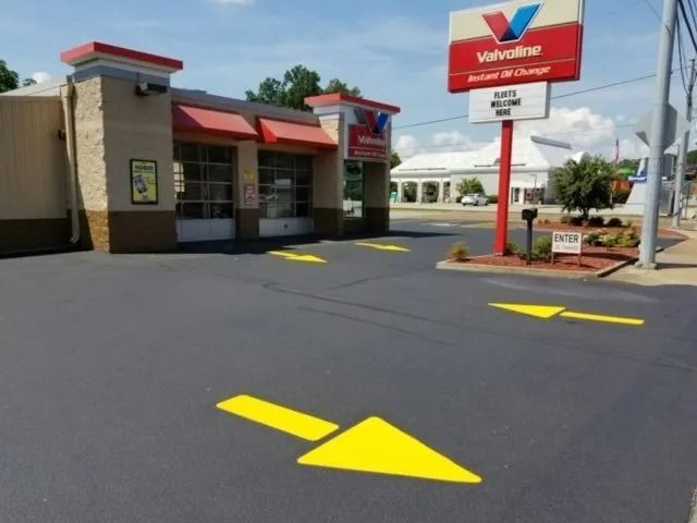 A Valvoline Instant Oil Change station with yellow directional arrows painted on a freshly paved asphalt parking lot.