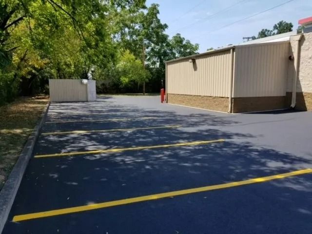 A freshly paved, empty parking lot with yellow painted lines alongside a building and a tan enclosure.