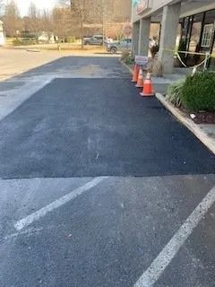 A rectangular patch of freshly paved black asphalt in an outdoor parking lot, marked by three orange safety cones.