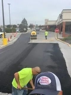 Paving crew working on a commercial parking lot with asphalt equipment and cones.