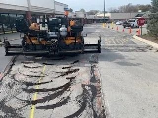 A construction paver sits on a parking lot surface marked with black asphalt streaks near a stop sign.