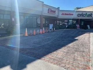 A row of storefronts featuring a State Farm and a Cricket Wireless, with orange traffic cones blocking a parking area.