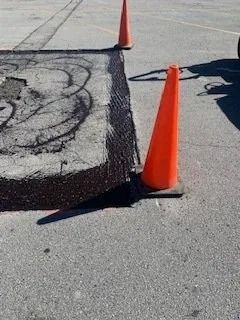 Two orange traffic cones mark a rectangular section of asphalt that has been milled and prepared for repair.
