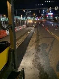 Nighttime view from a vehicle overlooking a road construction zone with orange barriers and fresh pavement.