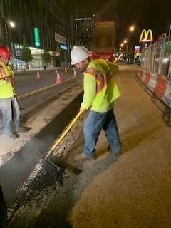 Construction workers in reflective vests and hard hats work on a paved road at night near a McDonald’s sign.