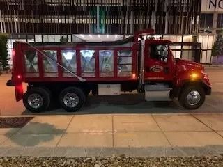 A red dump truck parked on a concrete sidewalk in front of a modern building with glass windows at night.