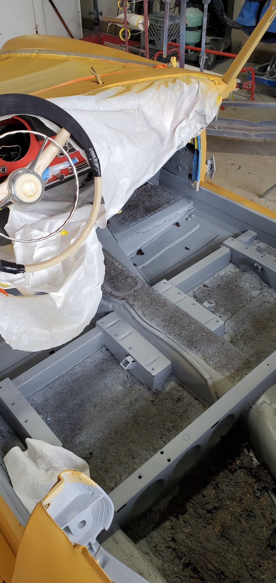 Interior of a classic car being restored, with painted metal floor and steering wheel.