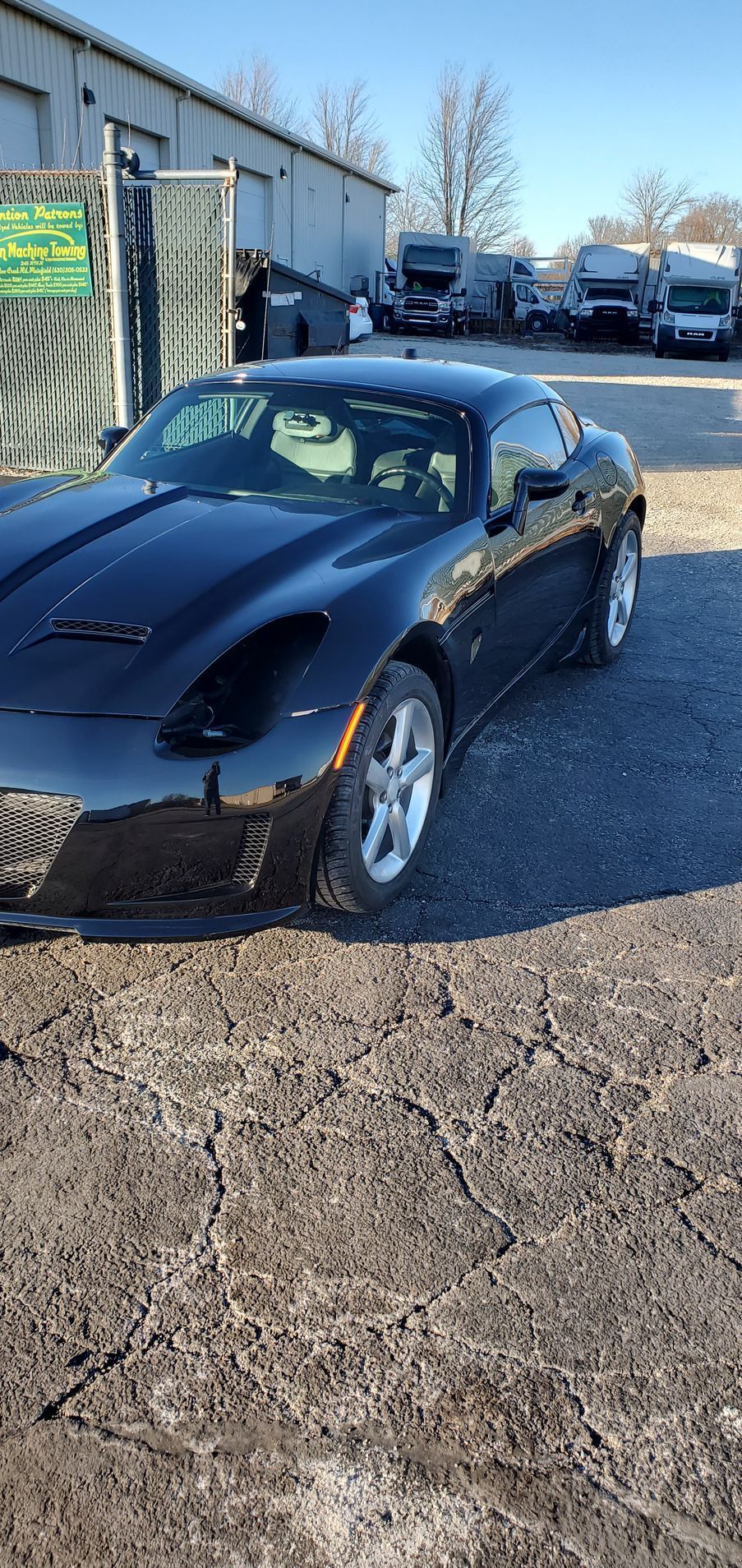 Black sports car parked outside a building, with other vehicles in the background. Bright, sunny day.